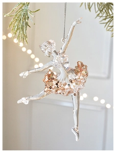 Detail of acrylic ballerina ornament with gold sequins on snow-covered pine branches