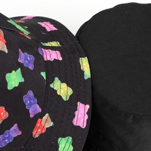 Macro detail showing colorful gummy bear patterns and fine stitching on the black cotton hat