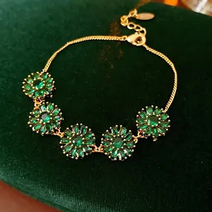 Vintage gold flower bracelet with green zircon petals on a dark green velvet display