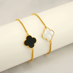 Elegant gold clover bracelet with black and white shell pendants on a white display