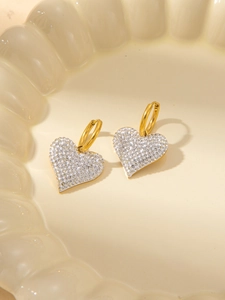 Elegant gold heart earrings with white crystals on a decorative ceramic plate