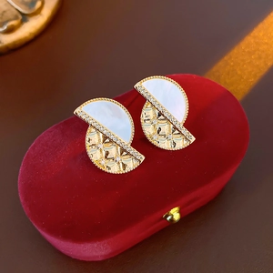 Detail of geometric earrings with white shell and gold diamond pattern on red velvet box