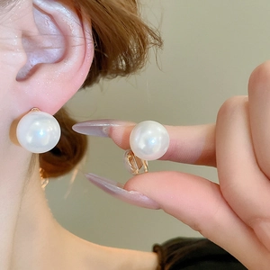 Detail view of large white round pearls on gold ear clips with soft silicone padding