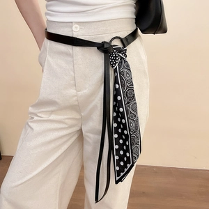 Detail of a thin black leather waist belt with a black and white printed silk scarf tassel