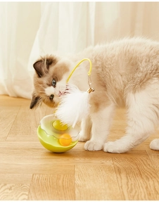 Ragdoll cat playing with yellow tumbler toy featuring white feathers and a small bell