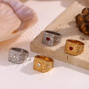 Detail of vintage heart charms on gold and silver sunburst rings on a wet stone surface
