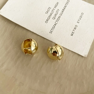 Macro shot of gold spherical stud earrings with a polished mirror finish on white paper