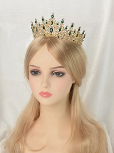 Detailed close-up of a golden girls' crown with sparkling green and clear rhinestones