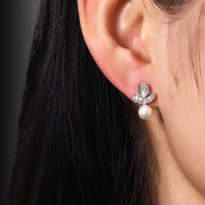 Macro shot of silver three-leaf pearl stud earrings with zircon inlay on a model