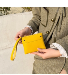 Close-up of a bright yellow leather coin purse with wristlet held by a model in a coat
