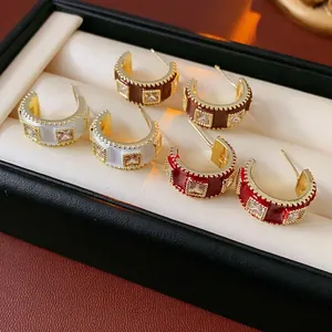 Three pairs of C-shaped gold-plated enamel earrings with crystals in white, brown and red