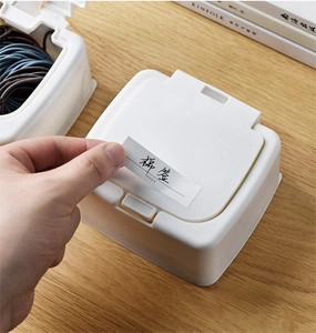 Close-up of a white desktop storage box with pop-up lid and label for organizing hair ties