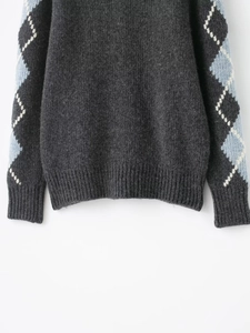 Detailed view of dark grey argyle knit sweater with blue and white diamond patterns