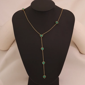 Detail of a golden Y-shaped necklace featuring six elegant green heart-shaped gemstones