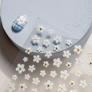 Macro shot of 3D embossed white daisy nail stickers with golden centers on a blue base