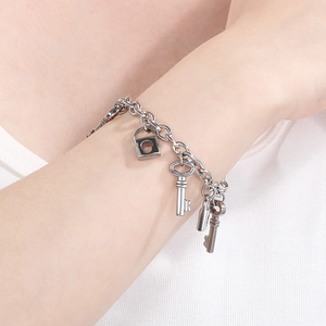 Detailed view of silver stainless steel chain bracelet with lock and key charms on wrist