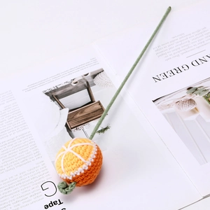 Close-up of orange knitted tangerine cat toy with green stick on a magazine