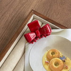 Macro view of a red acetate bow hair claw clip featuring elegant golden French lettering