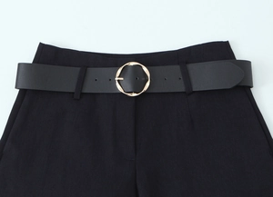 Close-up of a black leather belt featuring a unique twisted golden circular metal buckle