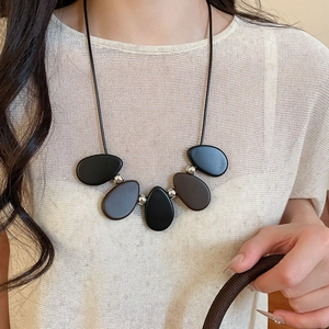 Modern long cord necklace with matte resin pebbles and metallic beads on knit sweater