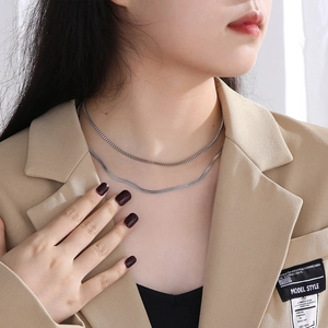 Close-up of layered silver box chain and flat snake bone necklace on a model's neck