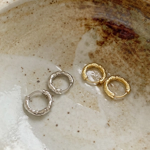 Detail of silver and gold hoop earrings with irregular hammered texture on ceramic