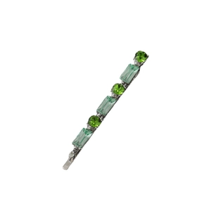 Close-up of green rhinestones in circular and rectangular shapes on silver hair clip