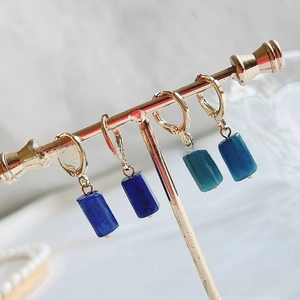 Detailed view of dangling rectangular gemstone pendants on gold metal hoops