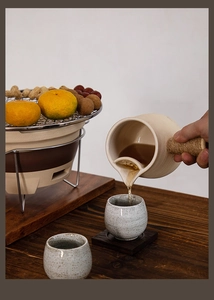 Close-up of ceramic tea pot and cups on grill with oranges and peanuts in cozy lighting