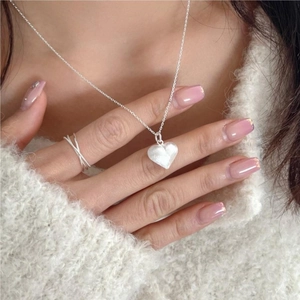 Detail of silver heart necklace and twisted rope ring on model wearing cream sweater