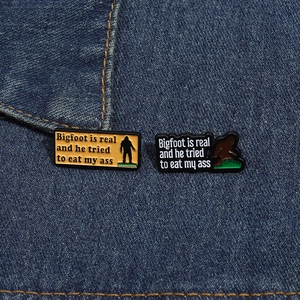 Set of two creative enamel Bigfoot pins on denim jacket showing humorous quote design