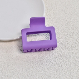 Detail view of square matte purple claw clip on textured background with ceramic plate