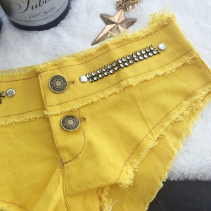 Detail der gelben Denim-Shorts mit silbernen Strasssteinen und Used-Look-Fransenrand