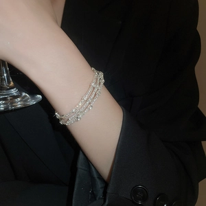 Dettaglio di un bracciale elastico multistrato argento con perle e cristalli al polso