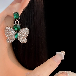 Détail d'une boucle d'oreille papillon en pierre verte carrée avec diamants scintillants