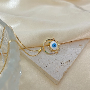 Golden Evil Eye pendant necklace with colorful zircons on silk and marble background