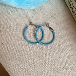 Macro shot of minimalist blue enamel hoop earrings on a beige textured fabric background