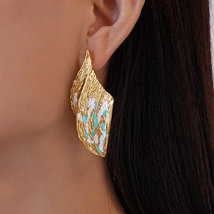 Detail of golden wrinkled leaf earring with blue enamel worn on a model ear