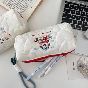 Macro view of white quilted pencil case with cute dog embroidery and pens inserted