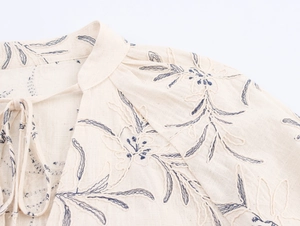 Detailed view of blue floral embroidery on apricot linen V-neck shirt with tassels