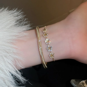 Detail of layered gold bracelet with zircon star flowers worn on wrist in warm light