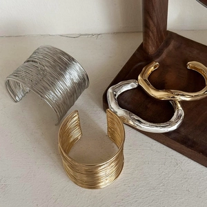 Minimalist wide irregular gold and silver open cuff bracelets on a wooden display
