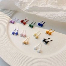 Collezione di piccoli orecchini a perno tondi in undici colori su un piatto bianco