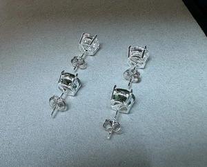 Detail view of classic four-prong silver studs with white and emerald green moissanite stones