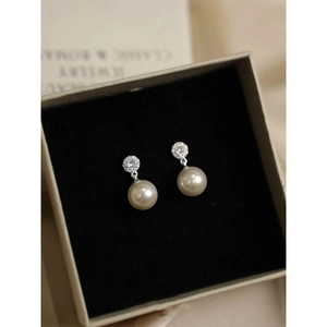 Macro detail of silver needle pearl drop earrings with sparkling zircon inlay in a box