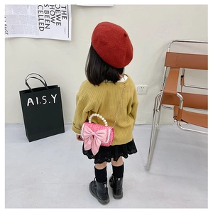 Rear view of child model wearing a pink tweed crossbody bag with bow and pearl handle