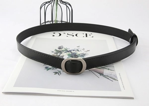 Detail of a minimalist black faux leather belt featuring a silver oval metal buckle