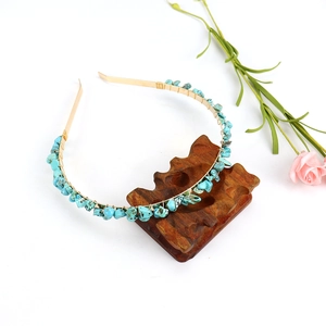 Close-up of handmade gold headband with turquoise stones on a dark wooden base