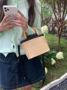 Outdoor shot showing straw bucket bag with wooden handle and black leather strap detail