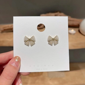 Elegant gold bow earrings with artificial pearls and crystals on branded nyunyu display card